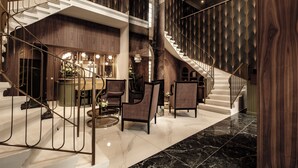 Un lobby espacioso con piso de mármol, una escalera en espiral y una zona de estar con sillas y una mesa.