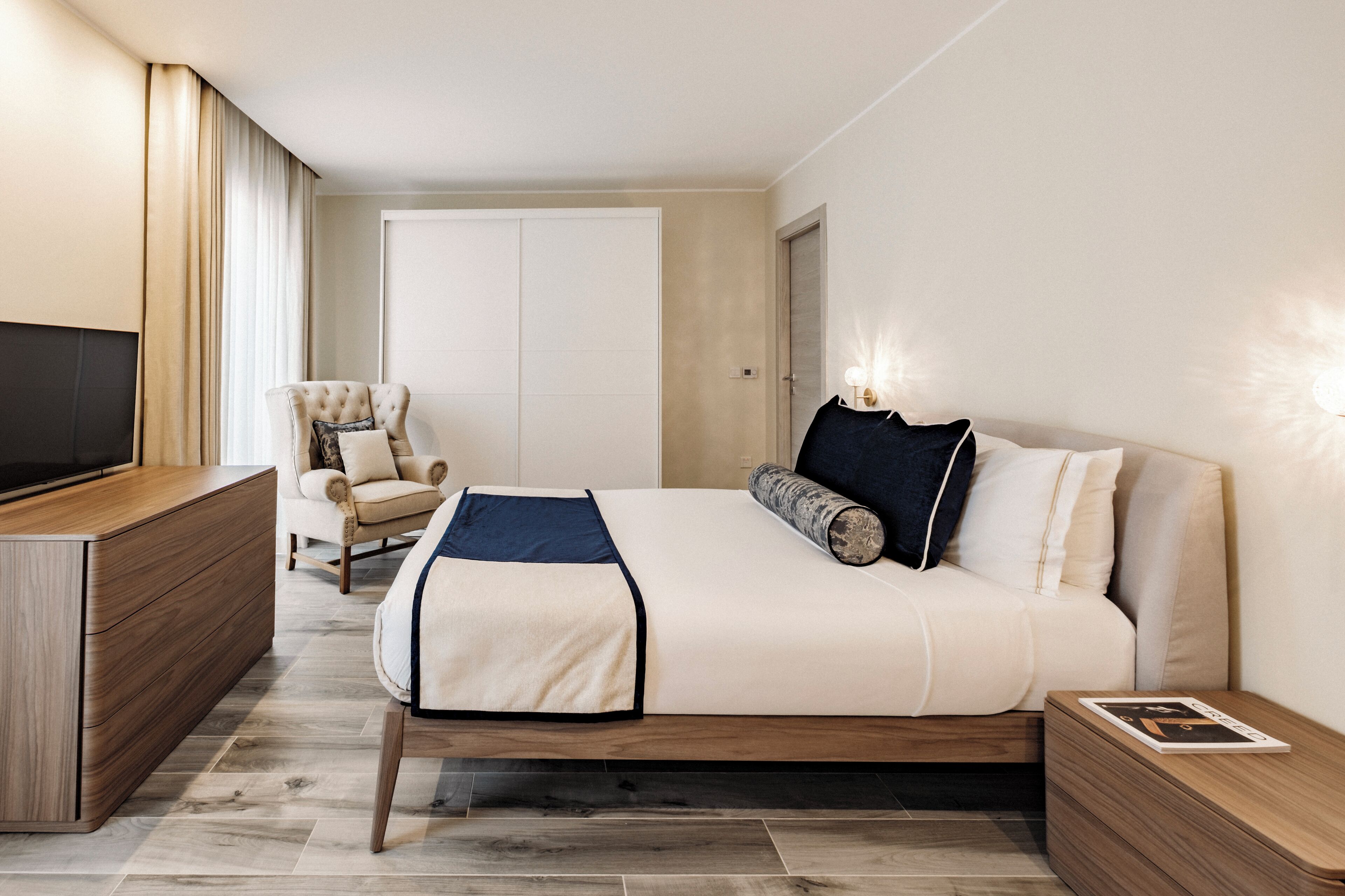 Una habitación de hotel moderna con una cama, una silla, un televisor y una mesita de noche.