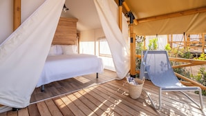 A wooden deck with a bed under a canopy, a chair, and a view of greenery. - wecamp Cádiz (Puerto Real)