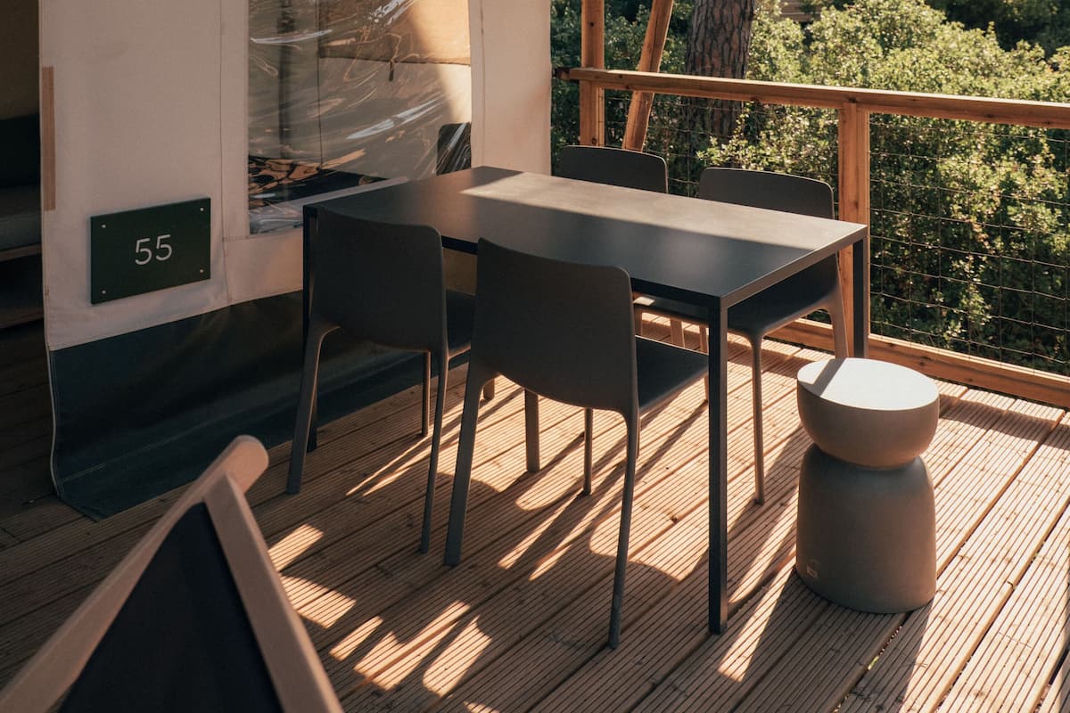 A wooden deck with a table and chairs, a number '55' sign, and a view of greenery.