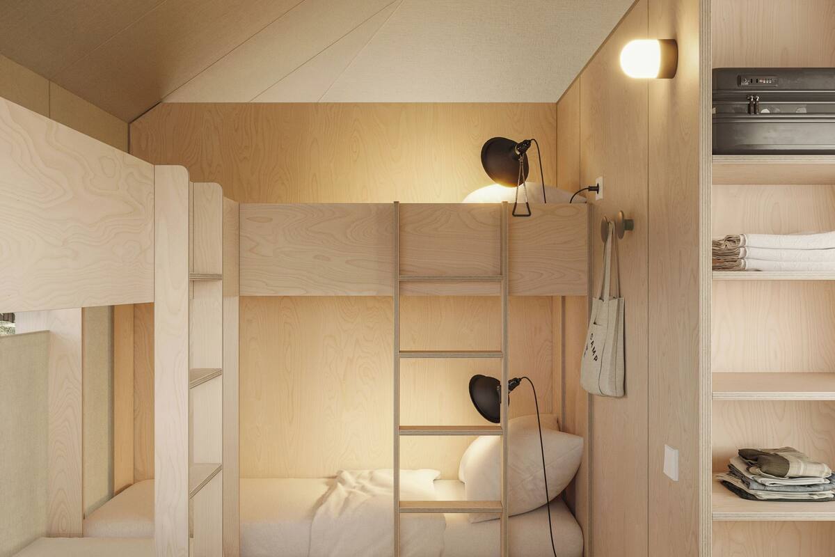 A compact, wooden room with bunk beds, a ladder, a desk, and a wardrobe.