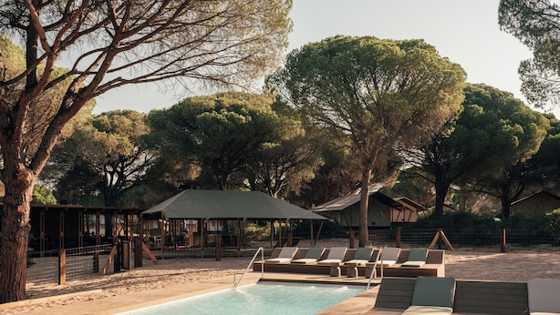 A pool area with lounge chairs and a covered seating area surrounded by trees. - wecamp Cádiz (Puerto Real)