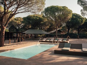 A pool area with lounge chairs and a covered seating area surrounded by trees. - wecamp Cádiz (Puerto Real)