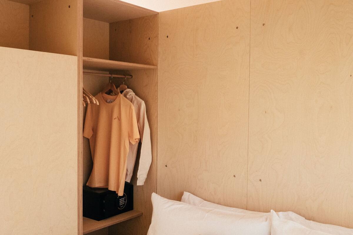 A bedroom with a bed, a green pillow, a wooden wardrobe, and hanging clothes.