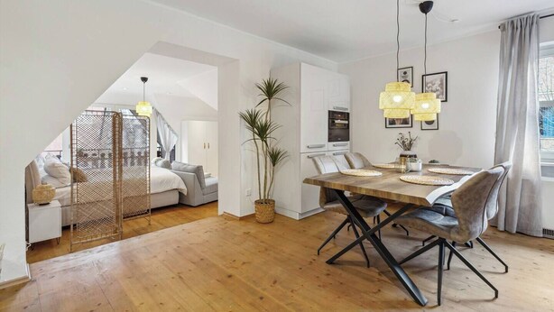 A modern interior with a dining area, a staircase leading to a loft bedroom, and a large potted plant. - Cozy half-timbered apartment in the center of Lüdinghausen with balcony (Lüdinghausen)
