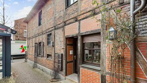 A brick building with a ground-level entrance, a visible number '34' on the door, and a parked white van with a logo. - Cozy half-timbered apartment in the center of Lüdinghausen with balcony (Lüdinghausen)