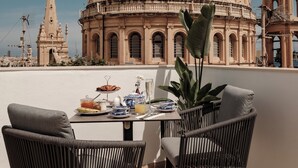 Una terraza con dos sillas de mimbre negro, una mesa con cosas para el desayuno y vistas a un gran edificio con cúpula.