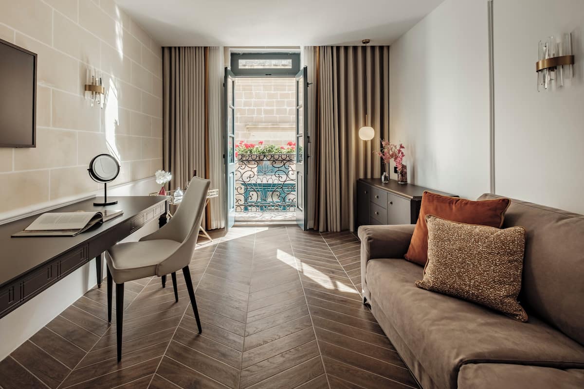 Una sala de estar moderna con un sofá, un escritorio y una silla. Hay un balcón con vistas a flores.