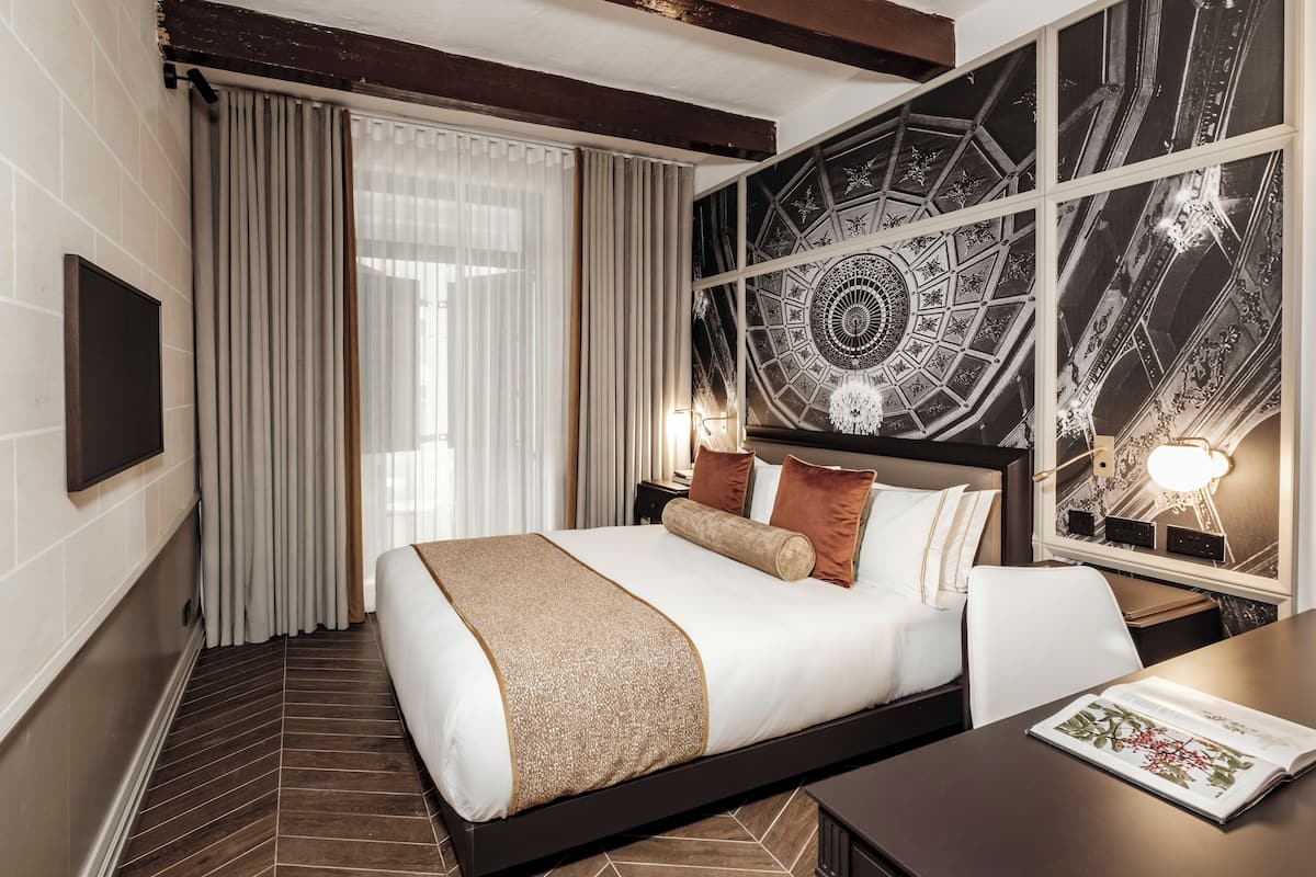 Habitación de hotel con una cama grande, un escritorio, una silla, un televisor y un adornado en la pared.