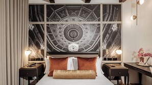 Una habitación de hotel moderna con una cama grande, dos mesitas de noche, un escritorio y un techo decorativo.