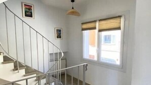 Eine Treppe mit Metallgeländern führt zu einer oberen Etage. Rechts daneben befindet sich ein Fenster mit Jalousien.