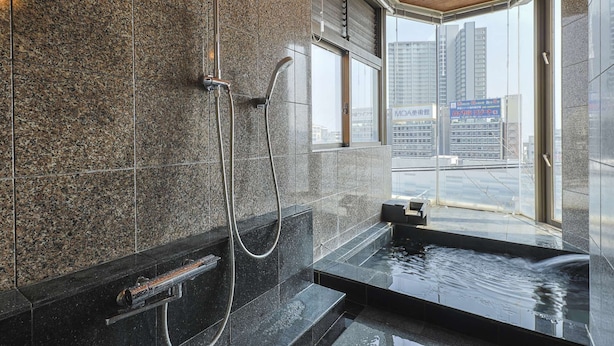 A modern bathroom with a granite wall, a shower, and a sink with a view of the city. - UNDER CURRENT ATAMI | Private Villa with Hot Springs & Fireworks View (熱海市)