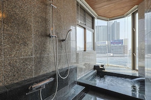 A modern bathroom with a granite wall, a shower, and a sink with a view of the city.
