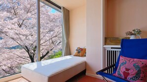 A room with a bed, a chair, a window with a view of cherry blossoms, and a radiator. - UNDER CURRENT ATAMI | Private Villa with Hot Springs & Fireworks View (熱海市)