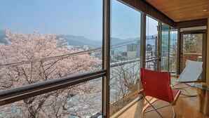 A modern interior with large windows, a red chair, and a view of cherry blossoms. - UNDER CURRENT ATAMI | Private Villa with Hot Springs & Fireworks View (熱海市)