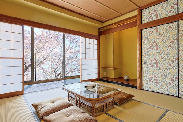 A traditional Japanese room with tatami flooring, a low table with cushions, and a sliding door with floral patterns.