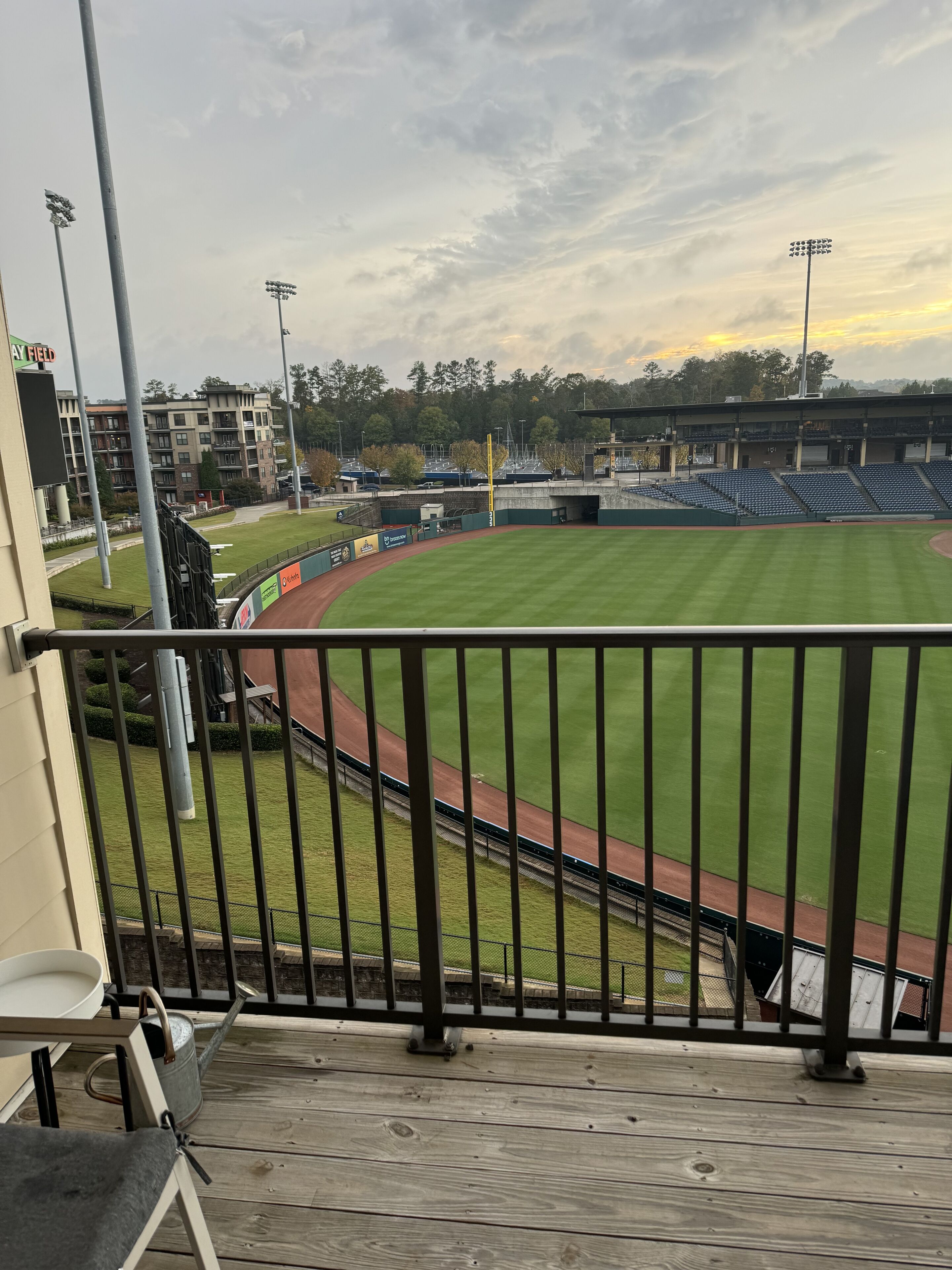 A view from a balcony overlooking a baseball field with a green outfield, a red infield, and a row of blue seats.