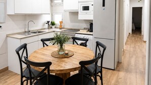 A modern kitchen with white cabinets, a central island with a wooden table and chairs, a microwave, and a refrigerator.