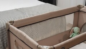 A child's playpen with a mesh top and a handle, placed on a carpeted floor next to a bed with a white headboard and a light fixture on the wall. - Apartment "Apartamento la Marquesa" embraced by the walls of Cordoba.  (Córdoba)