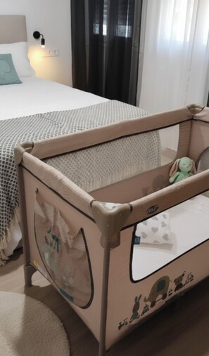 A child's playpen with a mesh top and a handle, placed on a carpeted floor next to a bed with a white headboard and a light fixture on the wall. - Apartment "Apartamento la Marquesa" embraced by the walls of Cordoba.  (Córdoba)