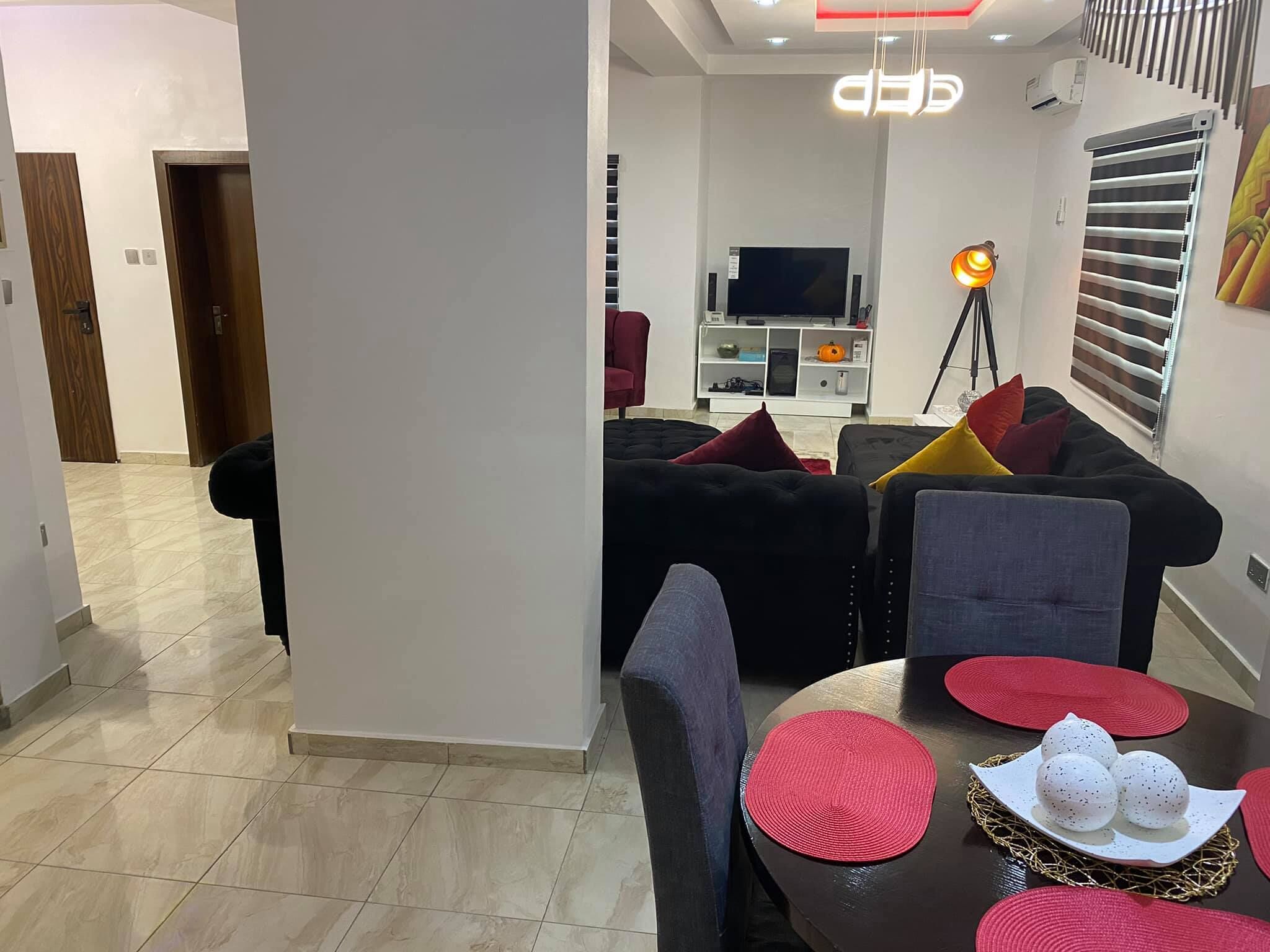 A modern living room with a sofa set, a dining table with placemats, and a television in the background.