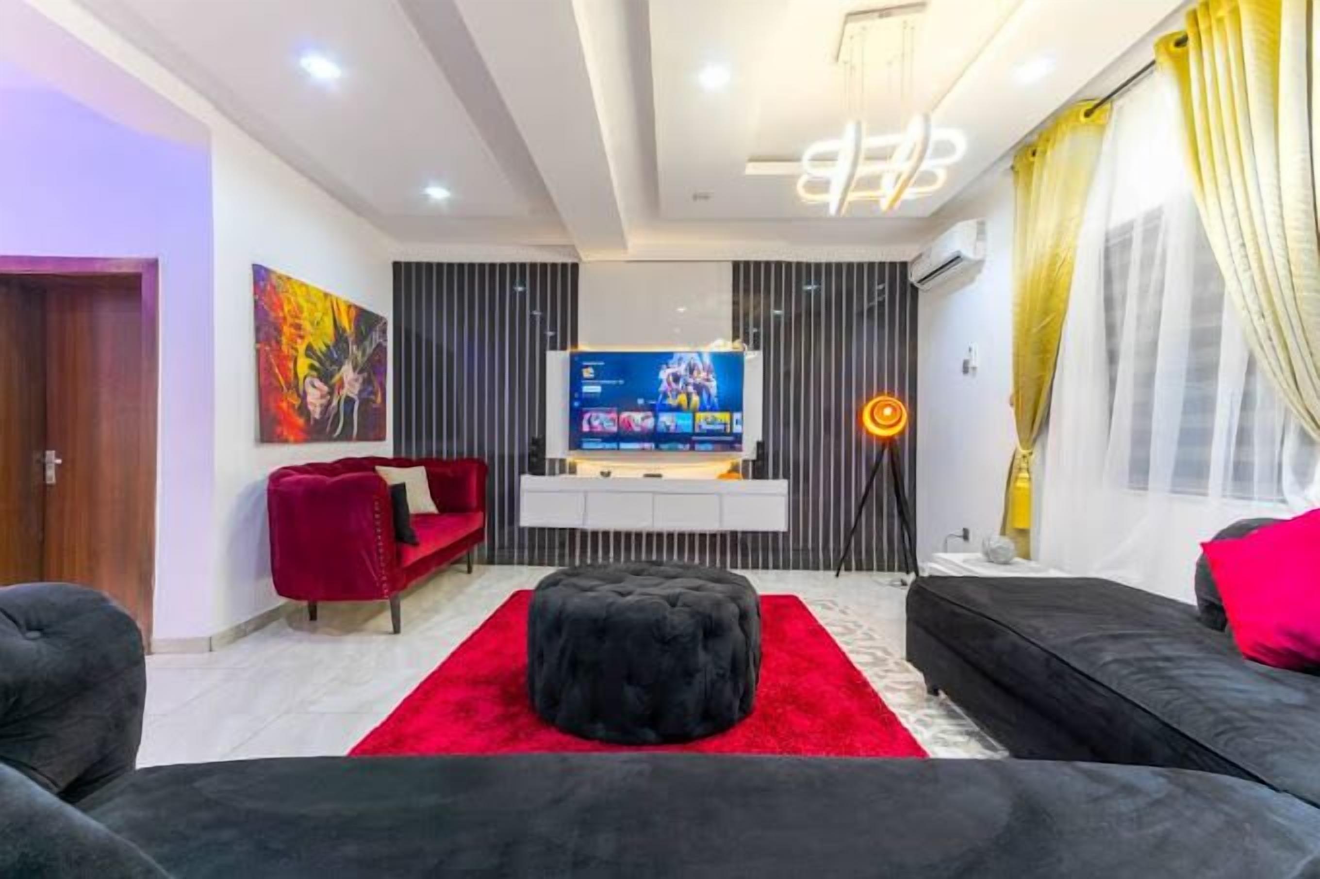 A modern living room with a red carpet, black ottoman, and a flat-screen TV on a white console.