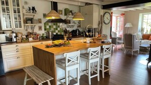 Una cocina con una isla de madera, taburetes de bar blancos y un banco. Hay armarios, un microondas y varios utensilios de cocina sobre las encimeras.