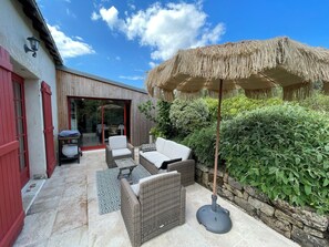 Eine Terrasse im Freien mit Korbmöbeln, einem Reetdachschirm und einer Steinmauer.