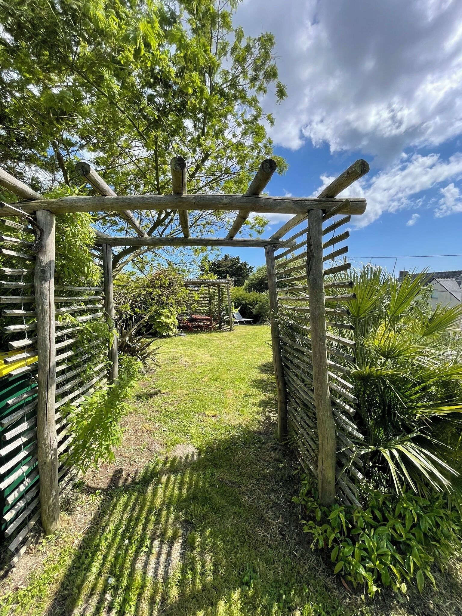 Una pérgola de madera en un jardín con césped y diversas plantas.