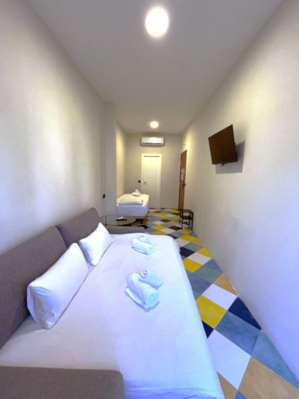 A hotel room with a bed, a sofa, a small table, and a TV mounted on the wall.