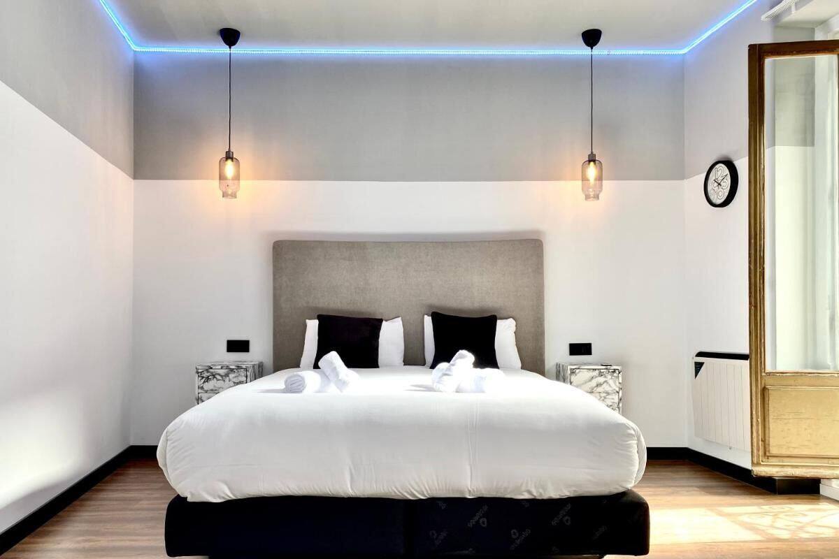 A modern bedroom with a large bed, two bedside tables, a headboard, and a clock on the wall.