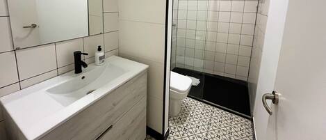A bathroom with a white sink, mirror, and black-tiled shower area.