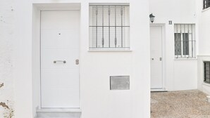 Un bâtiment blanc avec une porte fermée, une fenêtre avec des barreaux et une petite pancarte sur le mur.