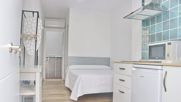 Une chambre d’hôtel de taille réduite, comprenant un lit, une kitchenette et un espace douche.