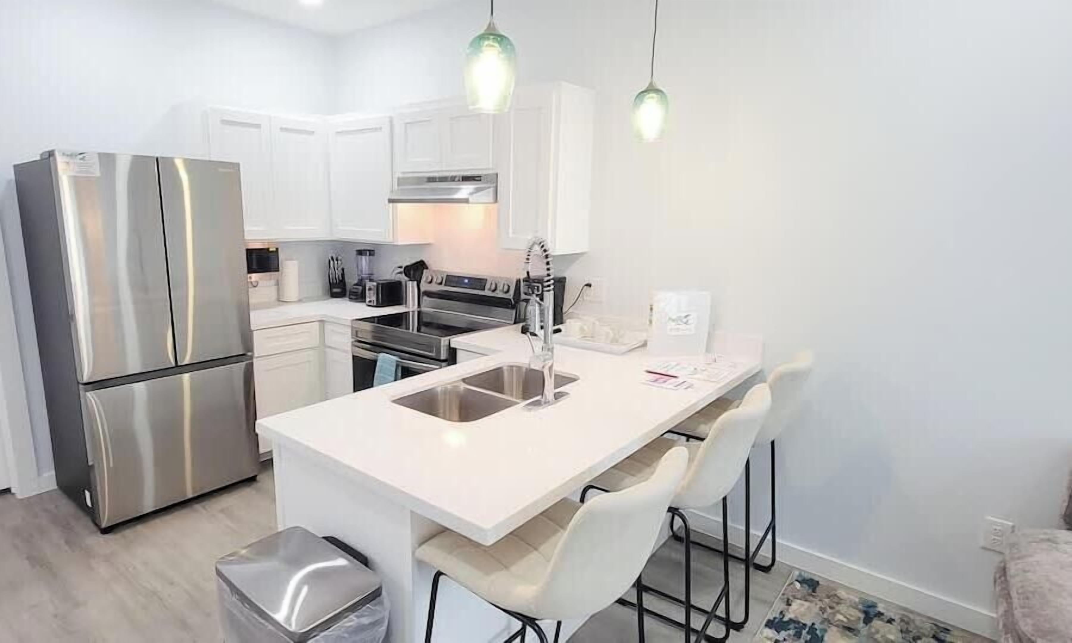 A modern kitchen with stainless steel appliances, white cabinetry, and a central island with bar stools.
