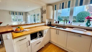 Una cocina moderna con armarios blancos, encimera de madera y horno integrado. Hay una ventana con vistas al exterior, y un lavamanos con grifo.