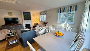 Una sala de estar con sofá, televisión, chimenea y mesa de comedor con frutero.