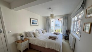 Un dormitorio con una cama grande, una mesita de noche con un florero, una silla y una ventana con cortinas.