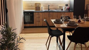 A modern kitchen with wooden cabinets, a black countertop, and a dining area with a table set for four. - Bonita cottage in Ada Bojana (Ulcinj Municipality)