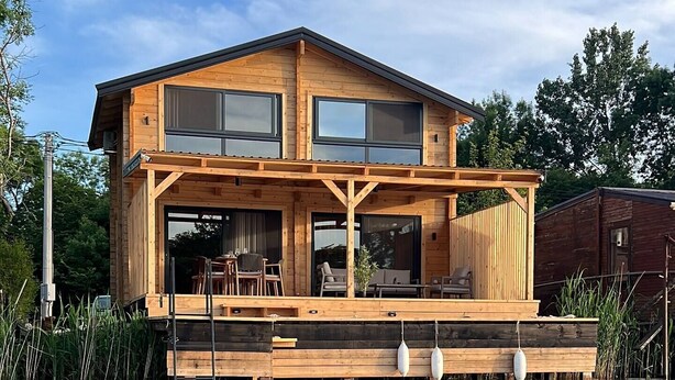 A wooden house with a deck over water, featuring large windows and a clear sky. - Bonita cottage in Ada Bojana (Ulcinj Municipality)