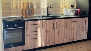 A modern kitchen with wooden cabinets, a built-in oven, a sink, and a countertop with various appliances. - Bonita cottage in Ada Bojana (Ulcinj Municipality)