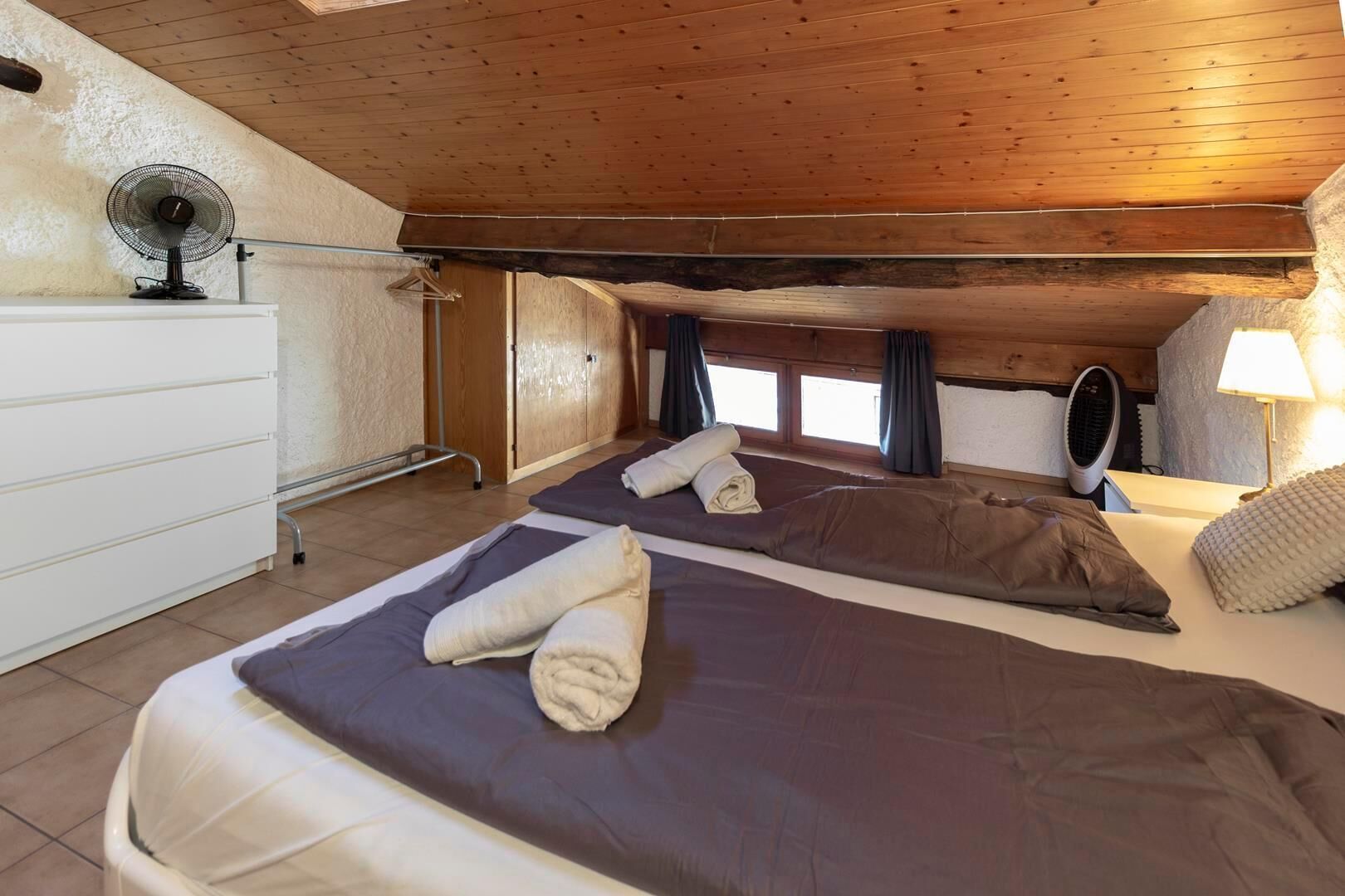A room with a bed, a dresser, a fan, and a window with curtains.