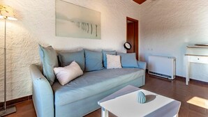 A cozy living room with a light blue sofa, a white coffee table, a painting on the wall, a clock, and a radiator. - Rustic Apartment First Floor (Castel San Pietro)
