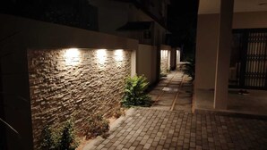 A nighttime view of a brick wall with embedded lighting, a paved pathway, and a gated entrance.
