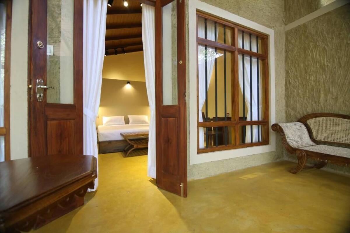 A room with a wooden bench, a bed, and a window with bars.