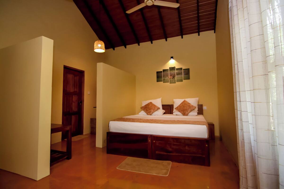 A bedroom with a bed, wooden headboard, ceiling fan, wall-mounted light, and a door.