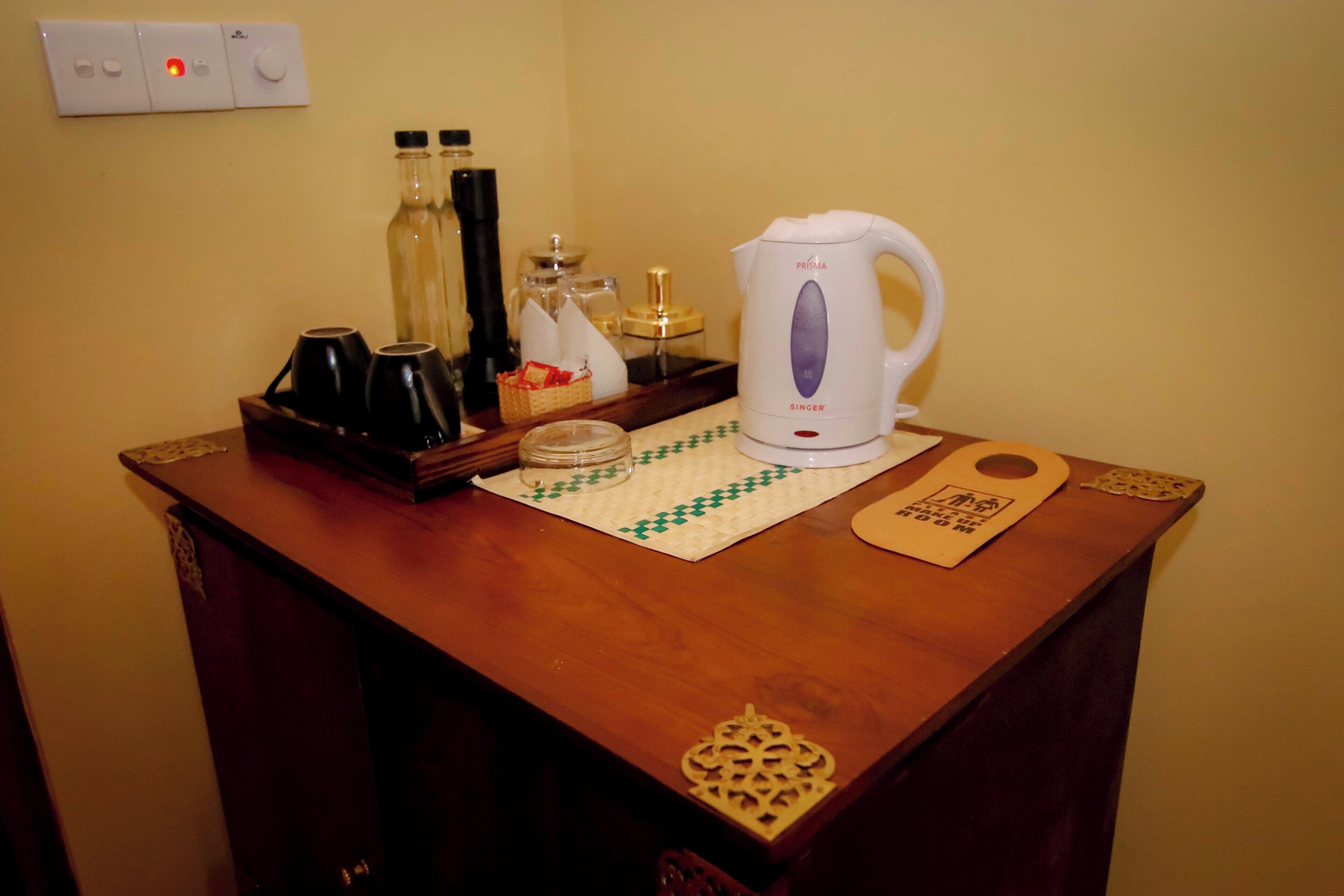 Una mesa de madera con una tetera, botellas, un vaso y una bandeja.