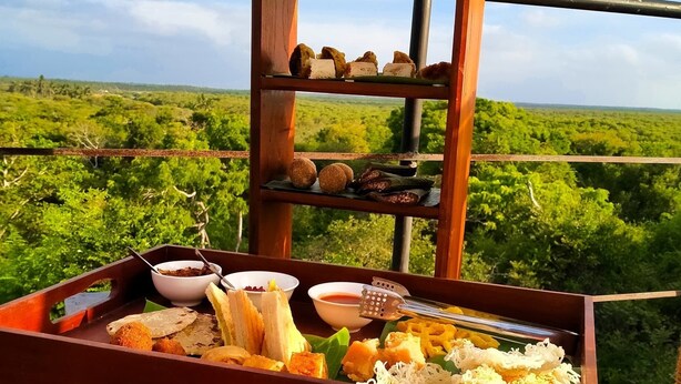 A dining table with a tray of food and a wooden rack with pastries, set against a lush green landscape. - Cloud Nine Lanka Resort Wilpattu (Wilpattu)