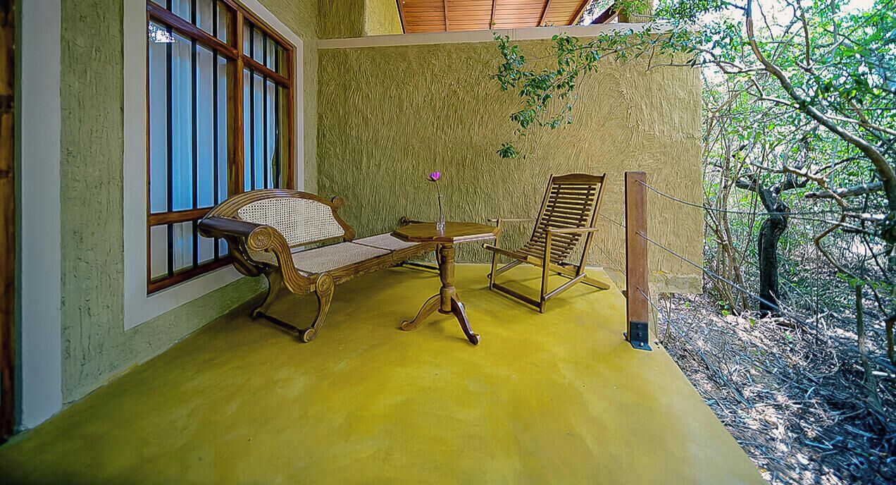A room with a bench, a chair, and a small table with a flower.
