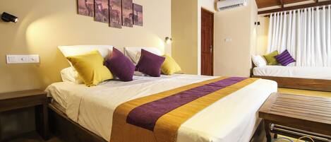 A hotel room with a large bed, a wooden bench, a bedside table, and a wall-mounted air conditioner.